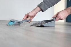 Man hands sweeping Dust with brush and dustpan, Housekeeping concept. Detail of man hands holding a broom and sweeping floor, collecting dust into a dustpan. Trash sweeping. 