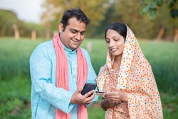 Happy indian rural farmer couple using smartphone to make online payment with debit card in agricultural field, shopping on internet with cellphone secure banking service system concept.