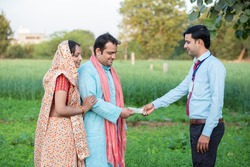 Young rural indian couple farmer receive money from banker at agriculture field.