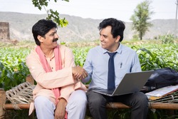 Happy smiling  rural indian male farmer hand shake with agronomist or banker use laptop sitting on bed at agriculture field. Deal final, Financial support or farming crop loan benefit