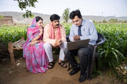 Happy rural indian farmer family with agronomist or banker use laptop. Man officer showing policy on computer screen, Financial support or farming crop loan,  husband wife with government scheme agent