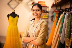 Portrait of Young happy indian woman, fashion designer tailor standing with crossed arms, measurement tape in garment workshop, seamstress, tailoring clothing on mannequin in  studio. skill india