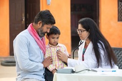 Indian female doctor with stethoscope checking little child patient heart beat or breath at village, Kid with his father getting examine by medical person, Rural India healthcare concept