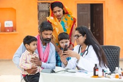 Young Indian Female Doctor with rural family give medicine outdoor village hospital,Healthcare government camp concept. Parents with two son getting medical help and support by pediatrician