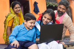 Happy young indian boy and girl using laptop. kids wearing school uniform holding computer with their parents behind them, online education and home schooling concept.