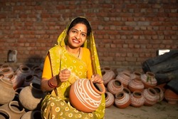 Portrait of happy traditional Indian woman potter artist painting and decorating design on clay pot for sale, handicraft, skill india.