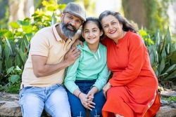Portrait of Happy indian senior people sitting with grand kid together in a park. Asian grand parents with grand daughter wearing casual cloths smiling, enjoying picnic holiday outdoor.