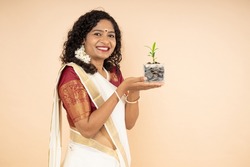 Happy South Indian woman holding jar filled with money saving coins and plant growing isolated on beige background. investment Concept