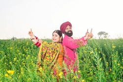 Happy Punjabi sikh couple doing bhangra dance in agriculture field celebrating Baisakhi or vaisakhi festival.