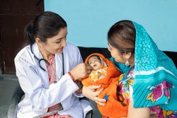 Indian pediatrician doctor examine new born baby at village, Mother wearing sari get infant check by medical person. Rural healthcare camp concept.