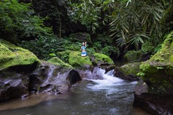 Young Caucasian woman sitting on the rock near the river in Vajrasana or Diamond pose. Hands hooked behind the back. Tropical nature landscape. Yoga retreat. Calm relaxing mood. Bali.