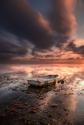 Old fisherman boat. Seascape. Fishing boat at the beach during sunrise. Low tide. Water reflection. Cloudy sky. Slow shutter speed. Soft focus. Vertical layout. Sanur beach, Bali, Indonesia.