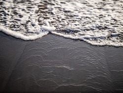 Wave close up on black sand beach. Waterscape background. Selected art focus. Black sand beach with white milky foam waves. Nature and environment concept. Black and white contrast. Copy space. Bali