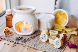 Using homemade mini wax melts in aromatherapy lamp diffuser at home interior concept. Melts making ingredients on table for unbleached beeswax, solid coconut oil, essential oil, dried flowers.