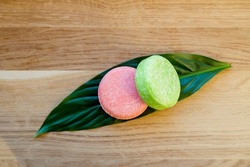 Pink and green color solid shampoo bars or conditioner bar on green leaf on wooden background. Minimalist beauty set indoors, copy space.