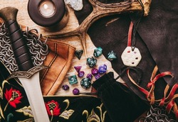 Fantasy role play board game still life concept. Background decorated with various character objects tools. Dagger, chain mail, amulet, clothing, dice set: D10, D20, D12, D6, D8.