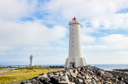 Akranes lighthouses on the west coast of Iceland. Bigger lighthouse is operational and smaller is deactivated old one. White building by the sea on sunny beautiful day.