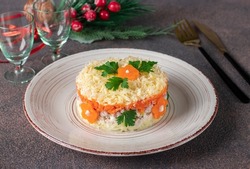 Layered salad with chicken, potatoes, carrots and cheese on a round plate on brown background