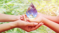 Earth in Water Drop image on baby and mother's hand on green blur background, World Water Day concept. Nature, clean, health, rain, environment. Elements of this image furnished by NASA.