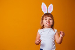 Little blond girl with dirty chocolate bunny ears eating Easter egg