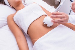 Cropped shot of a professional dermatologist performing radiofrequency lifting procedure on the stomach of a woman. Female client getting rf-lifting treatment on her belly at cosmetology clinic
