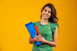 Smiling woman student with school books in hands on yellow background.