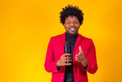 Cheerful Black Millennial Guy Holding Microphone And Singing At Camera, Young Joyful African American Hipster Man Enjoying Karaoke, Having Fun While Standing Over Yellow Studio Background, Copy Space