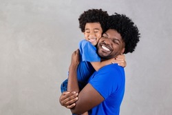 Portrait of handsome young african american father and his handsome son hugging, looking at camera and smiling. 