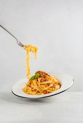 Eating pasta. Egg pasta tagliatelle with bolognese sauce made from meat and tomato sauce. Traditional italian dish from Bologna. Dynamic photo. Minimalism. Light grey background. Copy space.