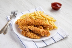 Homemade Crispy Chicken Tenders and French Fries on a white plate, side view.