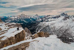Young male hiker alpinist with backpack on holiday in amazing dolomites landscape - Travel winter destination, Cortina snowy mountain in cloudy sky day

