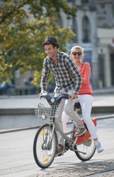 young couple in vacation having fun on a rental bike in the city, in summer