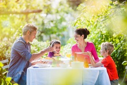 Summertime, nice family, Daddy, Mom and their two kids sitting at a table, eating lunch in the garden enjoying a sunny day