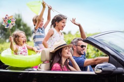 A joyful family, in a convertible car, goes on holiday to the sea. Children have colorful buoys and landing nets. Focus on the mother