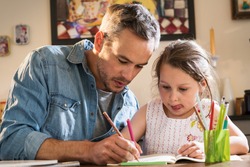 A father helps his little daughter to do her homework for the school.