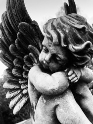 Close up of a little weathered angel statue on a grave stone. Black and white photo.