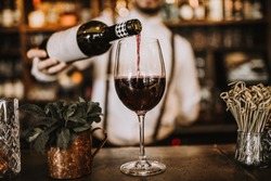 Bartender pouring red wine from a bottle in a wine glass, selective point of view on a wine glass
