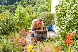 a young man in the garden in the rays of the summer sun tries to set fire to the grill Close up of a full frame on a green background