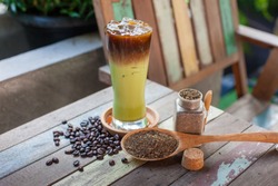 A glass of ice tea with tea powder and black coffee, tea powder in bottle and spoon, Iced green milk tea with hot coffee, coffee beans, two layer drink, mix drink. 