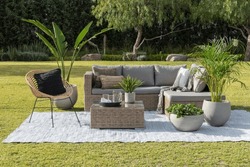 A contemporary outdoor patio space featuring a comfortable sectional couch, armchairs, decorative pillows, lush green grass