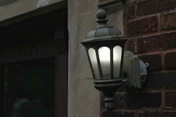 Beautiful cast iron street lamp hanging on a wall and glowing in the dusk.