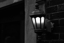 Beautiful cast iron street lamp hanging on a wall and glowing in the dusk in a black and white monochrome.