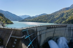 Water Turbines Are Producing Electricity At Power Plant. Panorama View Of Hydro Power Station And People On The Kurobe Lake Dam,Toyama. River Dam and Tateyama Mountains.