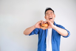 Attractive Asian man in casual shirt holding beef burger standing over white background, copy space. Happy man with burger.