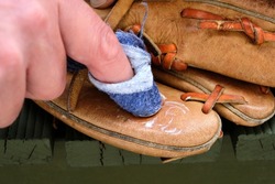 Applying leather conditioner to an old leather baseball glove with a blue rag