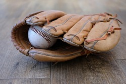 An old baseball inside an old well loved leather baseball glove, sitting on wooden floorboards