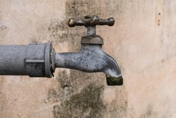Close up metal water spigot against old concrete wall with black mildew