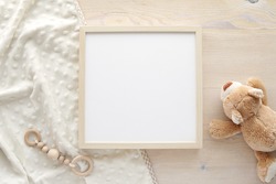 Wooden square frame mockup, empty frame mock up for nursery, baby room artwork, photo, sayings, flat lay composition with baby blanket, teddy bear and baby teether.    