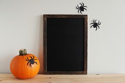 Wooden frame blackboard mockup for Halloween art, dark wood sign, chalkboard, pumpkin, paper spiders decorations.