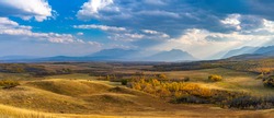Vast prairie and forest in beautiful autumn. Sunlight passing blue sky and clouds on mountains. Fall color landscape background. Waterton Scenic Spot, Waterton Lakes National Park, Alberta, Canada.